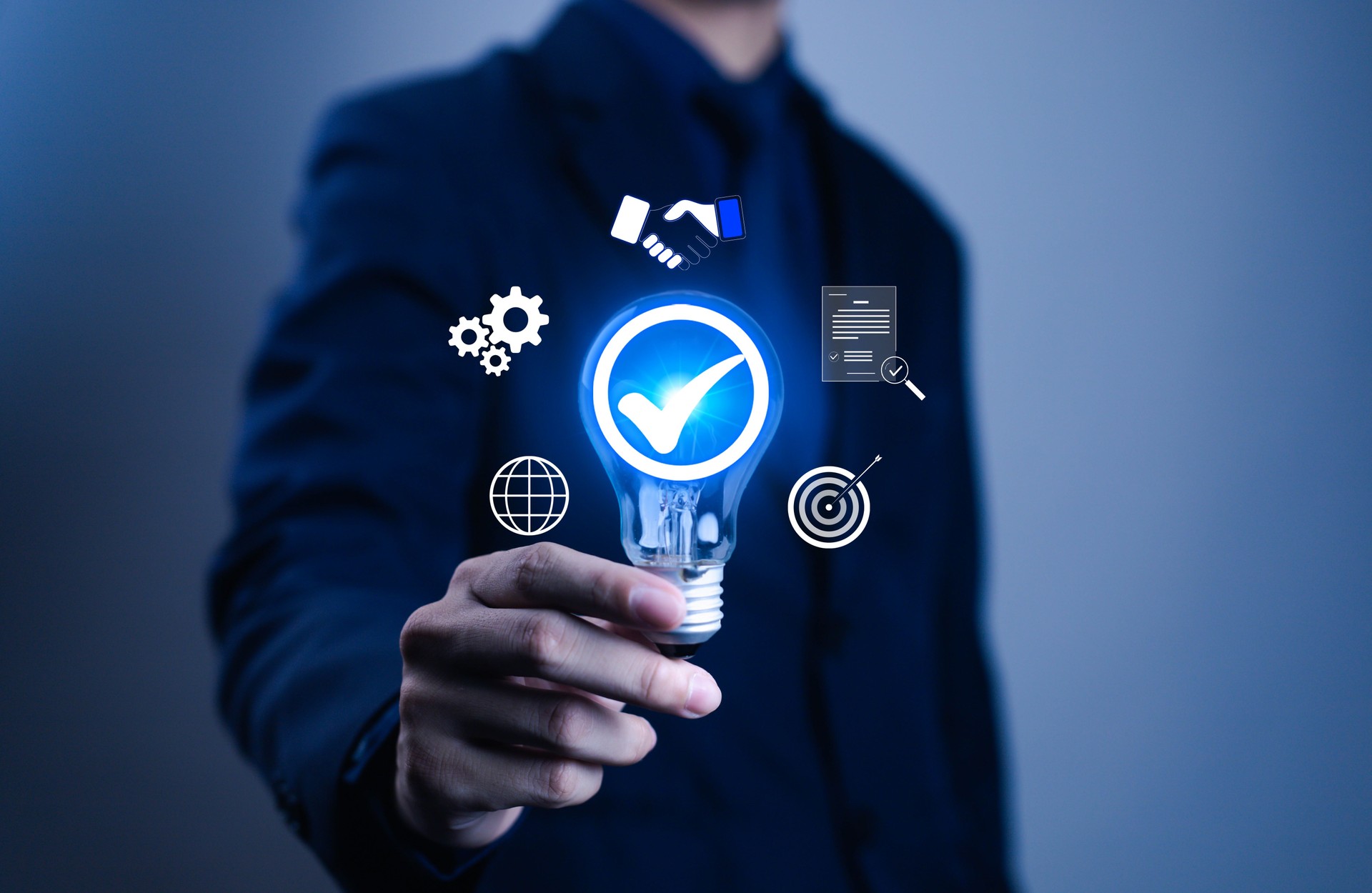 Businessman hand holding glowing light bulb with check mark icon, symbolizing innovation, business success, quality assurance, target achievement, teamwork, global connection, and smart solution.