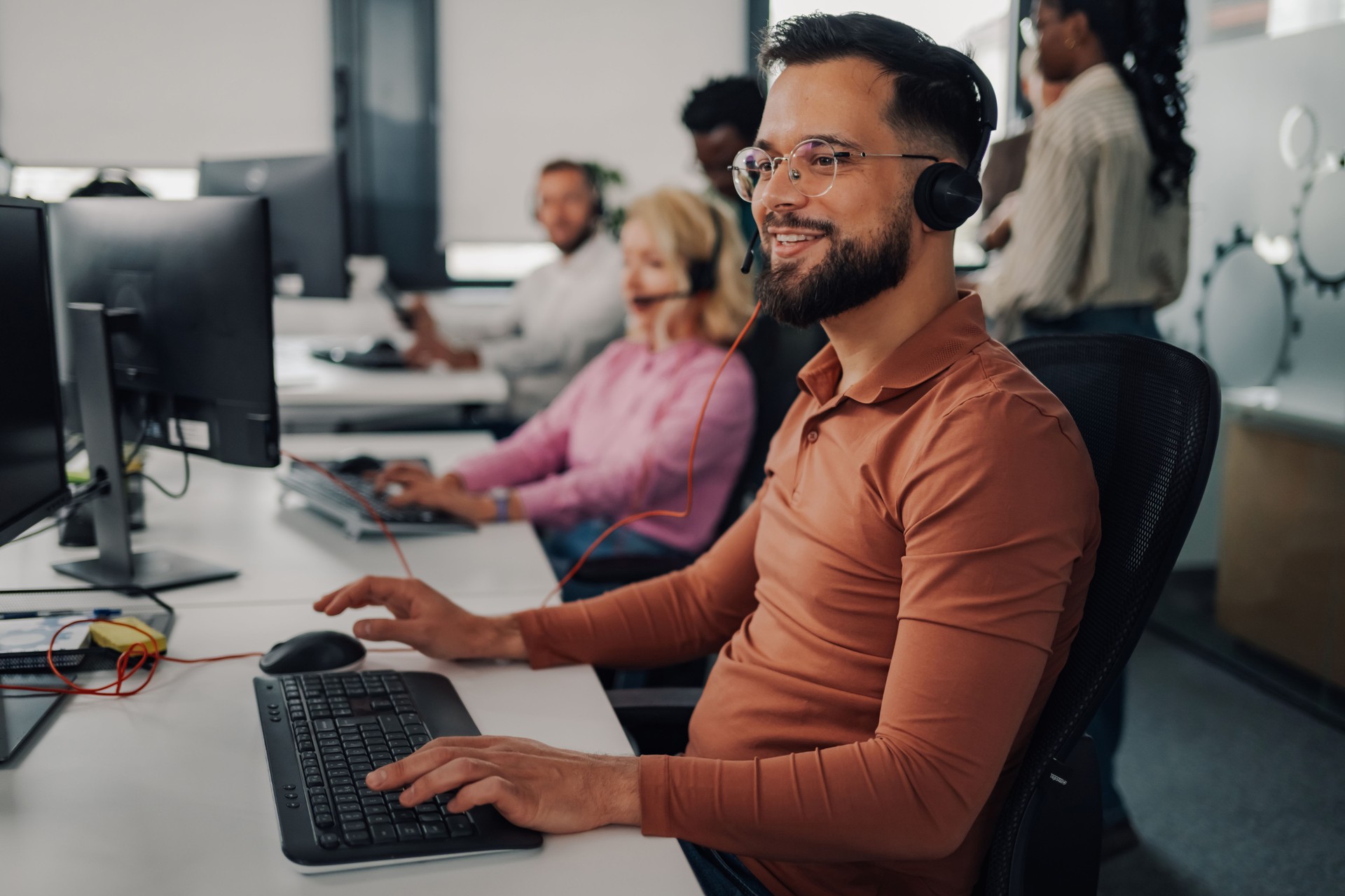 Male call center agent working on computer in busy office